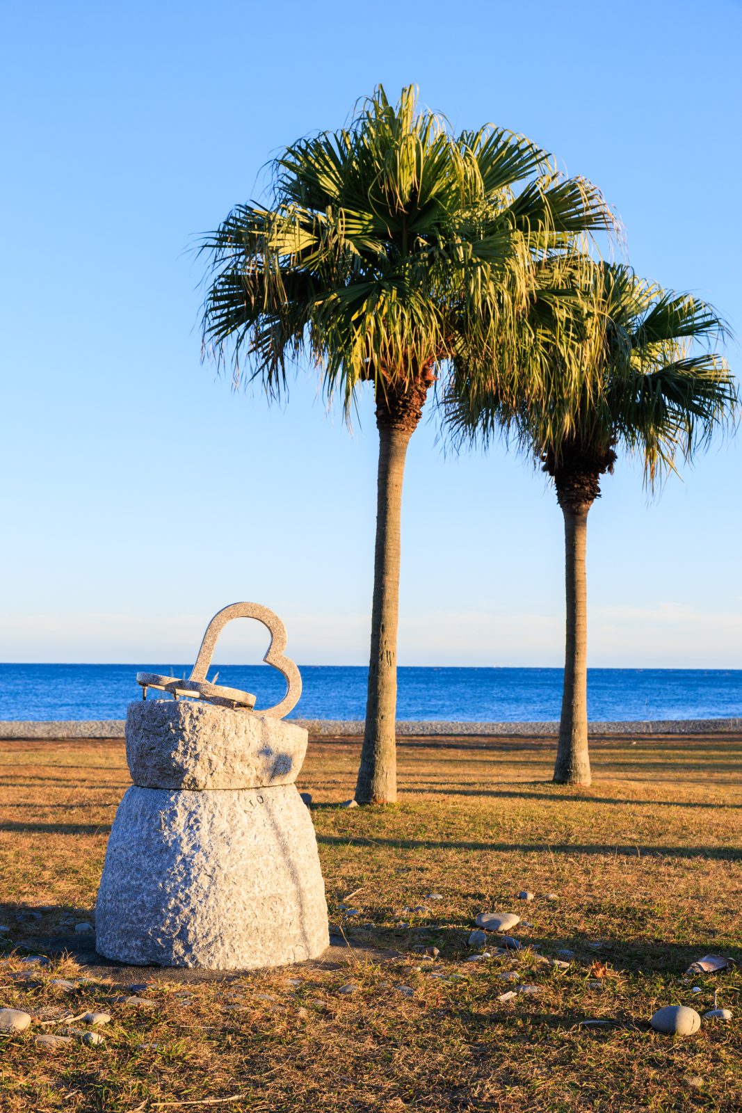 無料スマホ壁紙 ハートのモニュメントとヤシの木が並ぶサンセットビーチ。AndroidとiPhoneに対応した4K高画質の無料待ち受け画像。三重県御浜町の七里御浜ふれあいビーチで撮影したフリー写真素材