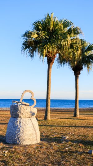 無料スマホ壁紙 ハートのモニュメントとヤシの木が並ぶサンセットビーチ。AndroidとiPhoneに対応した4K高画質の無料待ち受け画像。三重県御浜町の七里御浜ふれあいビーチで撮影したフリー写真素材