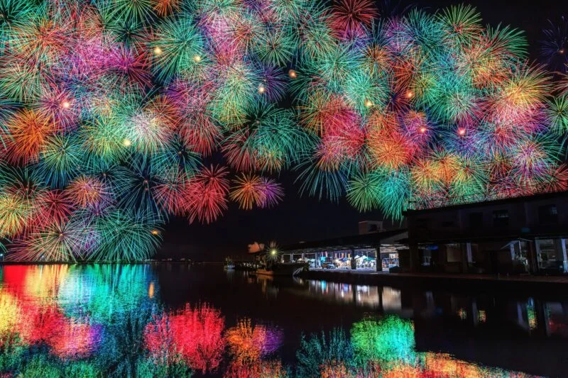 漁港でアーチを描く虹色の花火（三重県尾鷲市・おわせ港まつり）