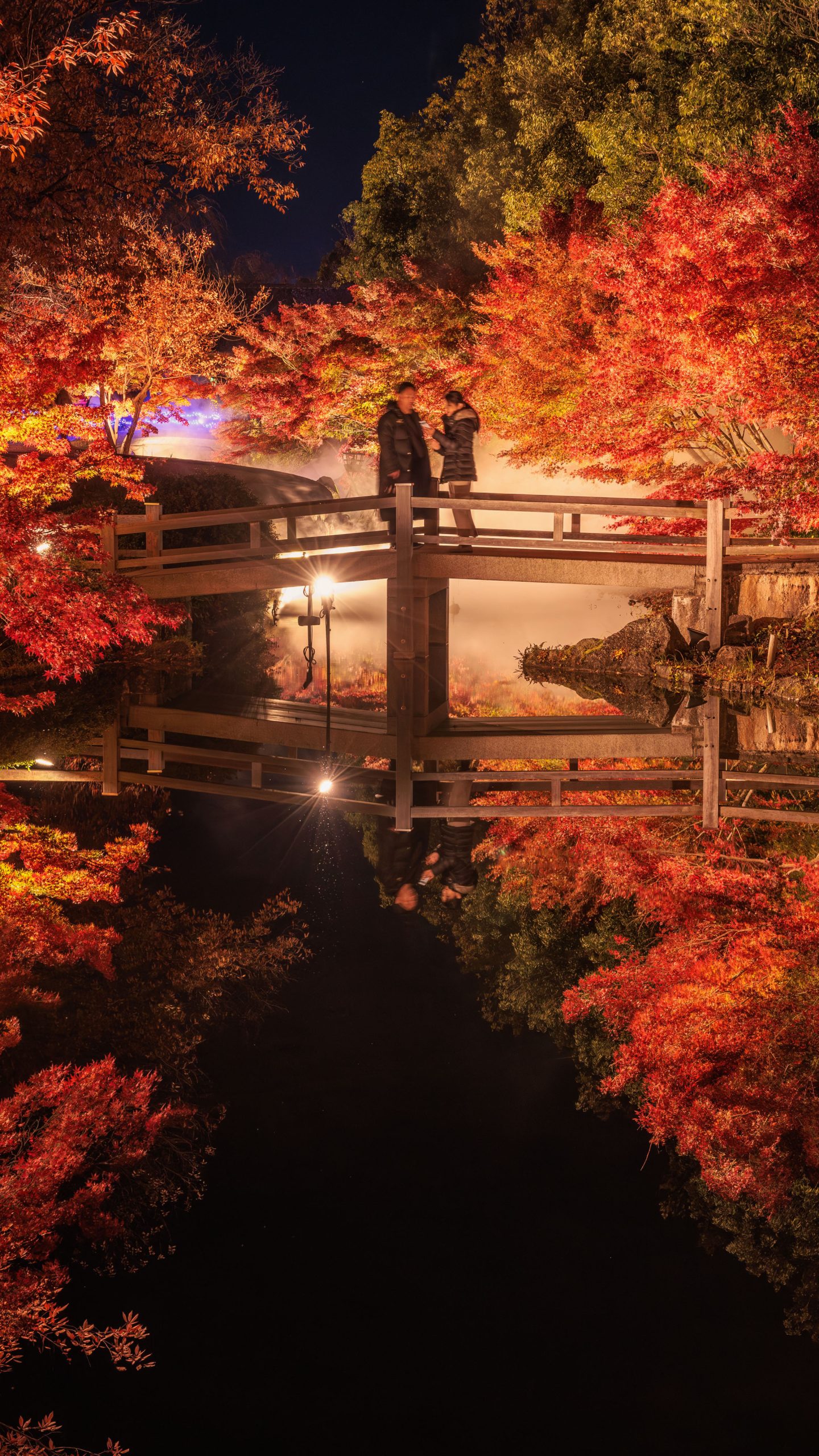 鏡池の紅葉ライトアップを橋から眺める人(三重県桑名市・なばなの里)